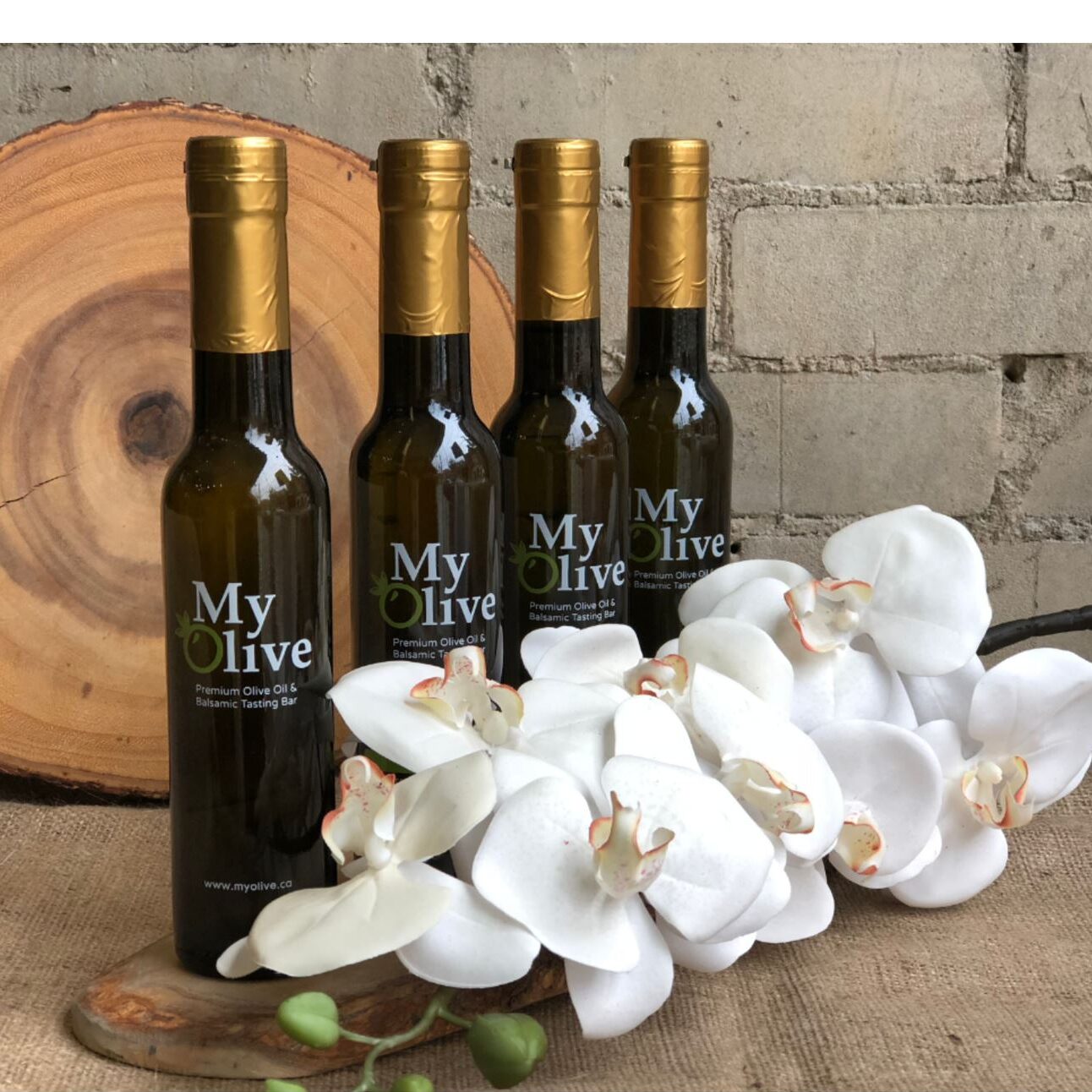 Image of four bottles of My Olive olive oil in succession with some orchids in the foreground.