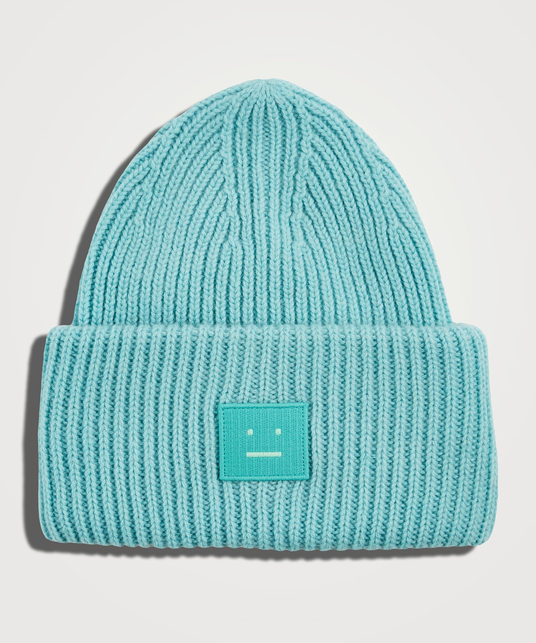Image of a ribbed Acne Studios teal toque with the Acne Studios logo on the cuff.