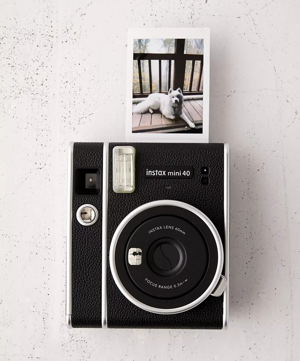 Image of a black and silver instax mini 40 with a photo printout of a samoyed sitting on a deck above it.