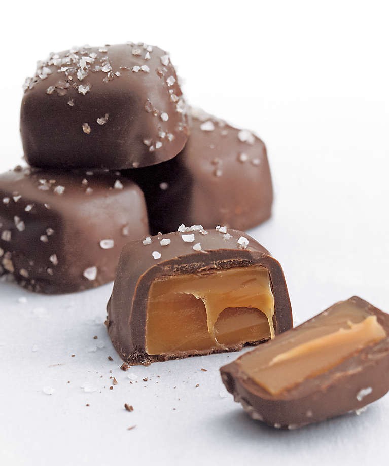 Close-up of four sea salt caramels from Crate&Barrel. There are three stacked chocoaltes in the background and in the foreground, the chocolate is cut in half to show the caramel inside.