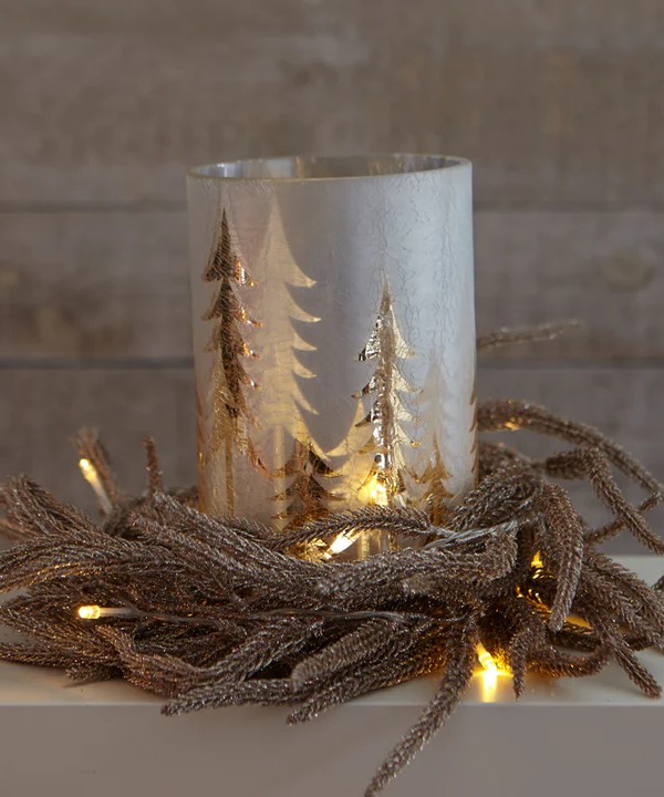 Image of a Christmas-themed candle with gold Christmas trees on it. There is some sort of garland at the base of the candle.