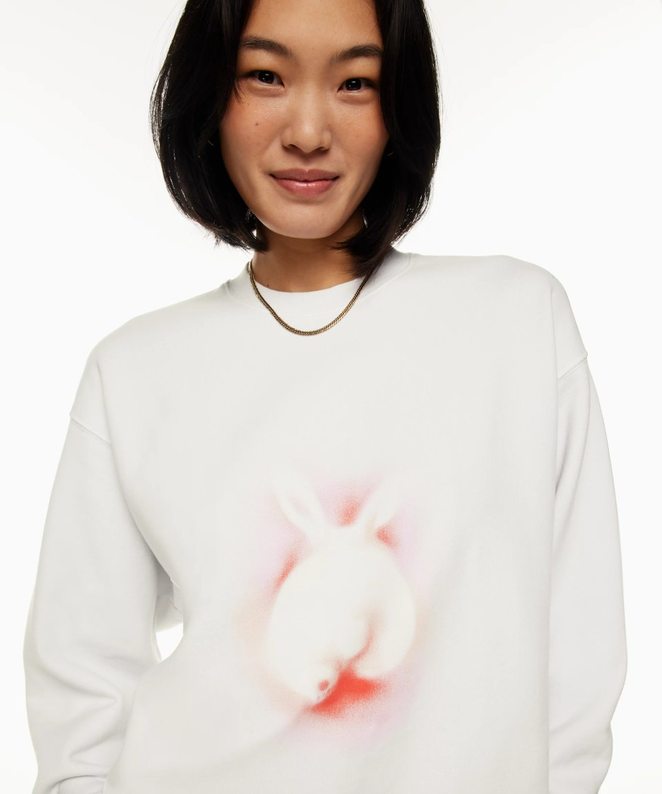 Close-up image of a model wearing a white Aritzia crewneck sweater with a bunny spray painted on the front.