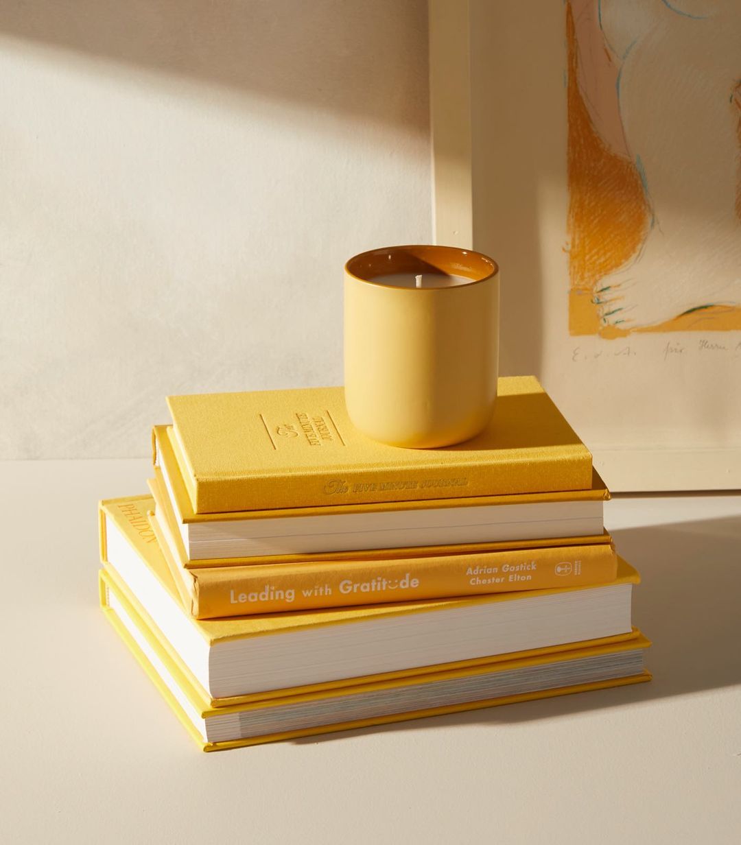 There are five yellow books stacked on top of each other with a small yellow candle sitting on top of the books.