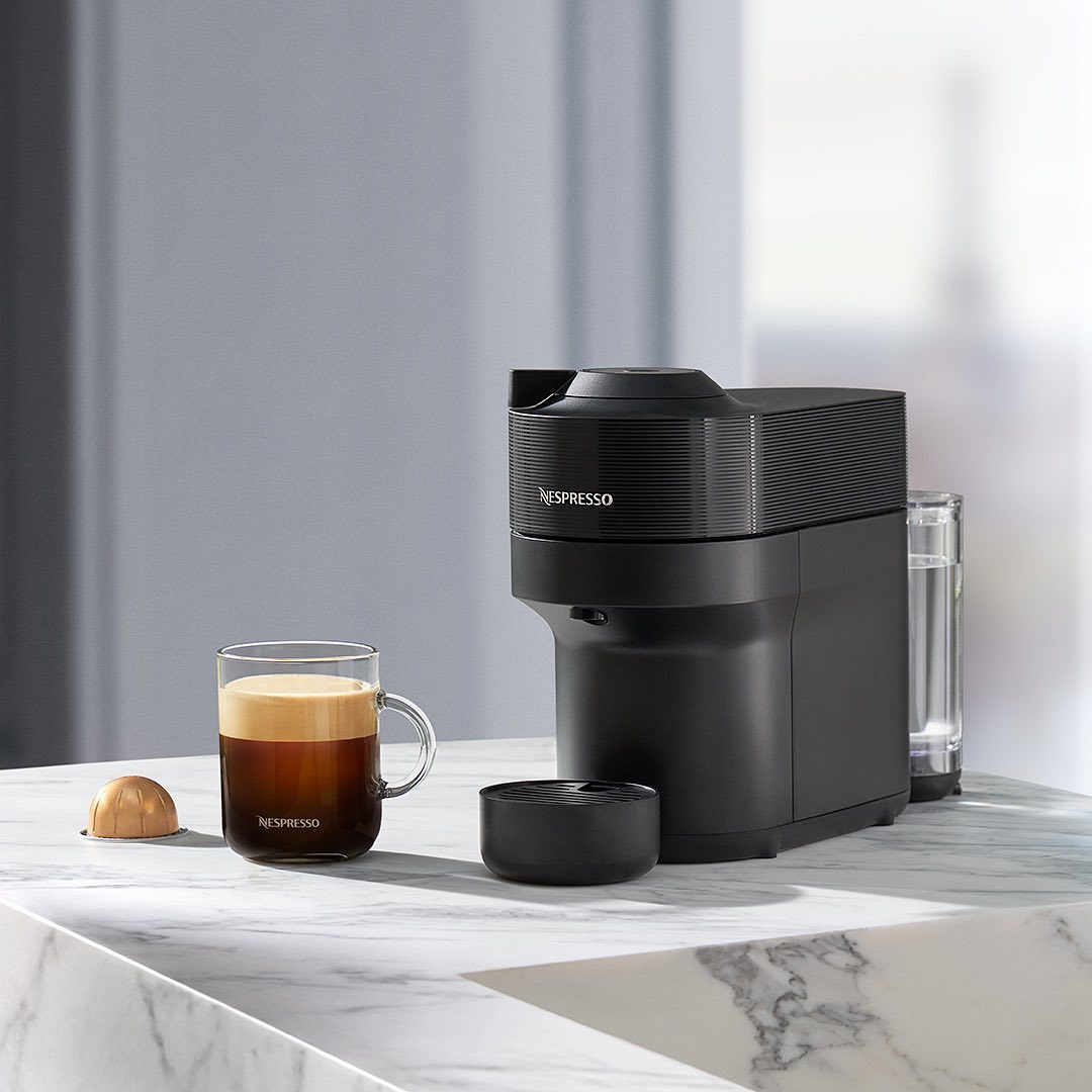 Nespresso machine sitting on marble countertop with a full espresso and pod sitting beside it.