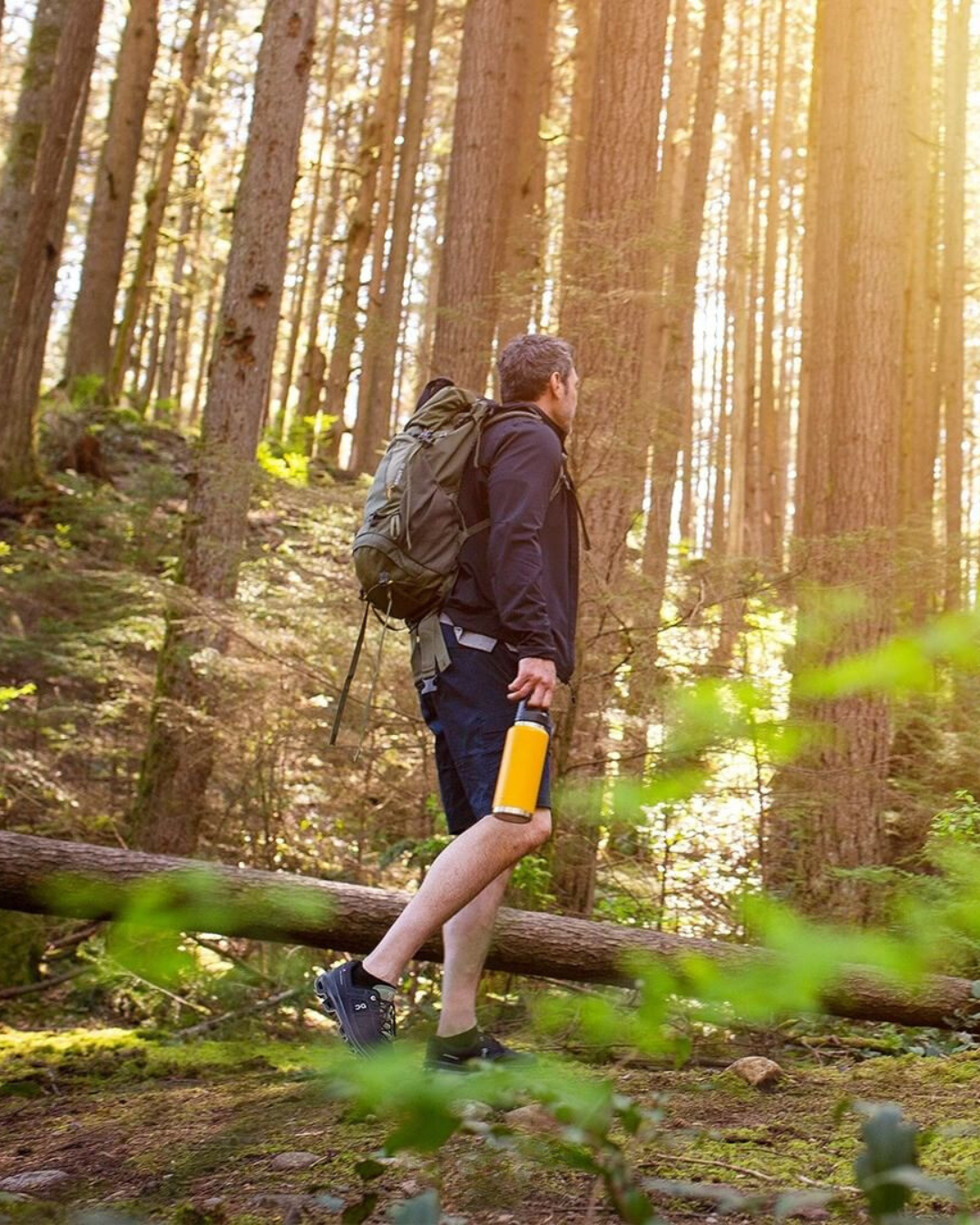 A man hiking in the woods holding a yellow water bottle