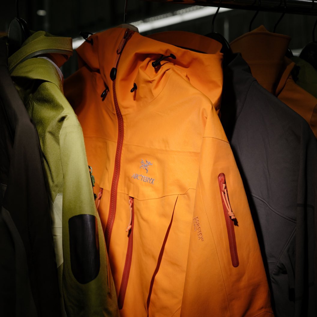A dark image of jackets on a rack. In the centre is an orange anorak that is illuminated by a flash of light.