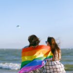two people sitting on a log with a Pride flag