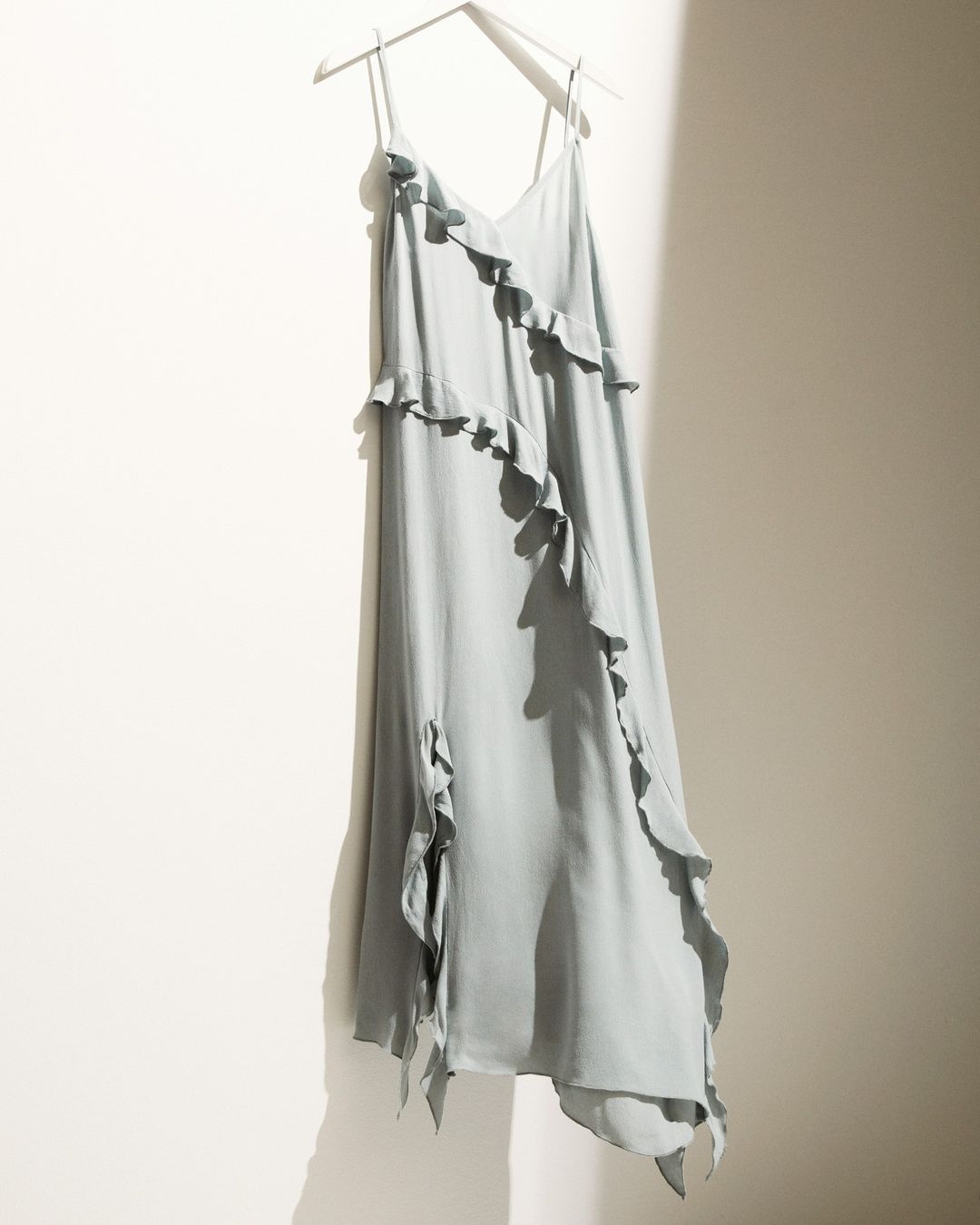 lifestyle image of a seamoss ruffled asymmetrical dress from H&M hanging on a hanger against a white wall