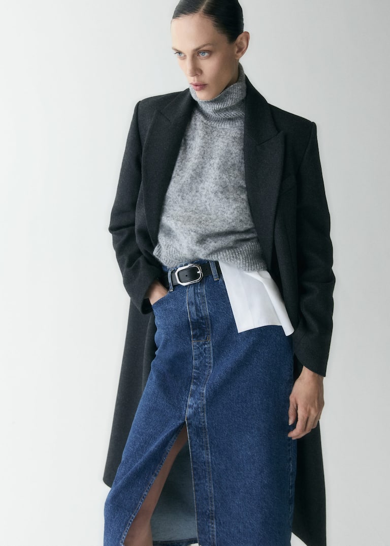 Model wearing a grey turtleneck, a black long coat, a black leather belt and a jean skirt from Mango