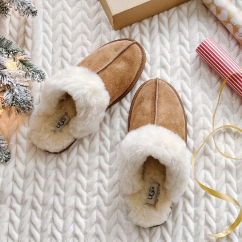 A pair of fur-lined slippers on a carpet next to a Christmas tree