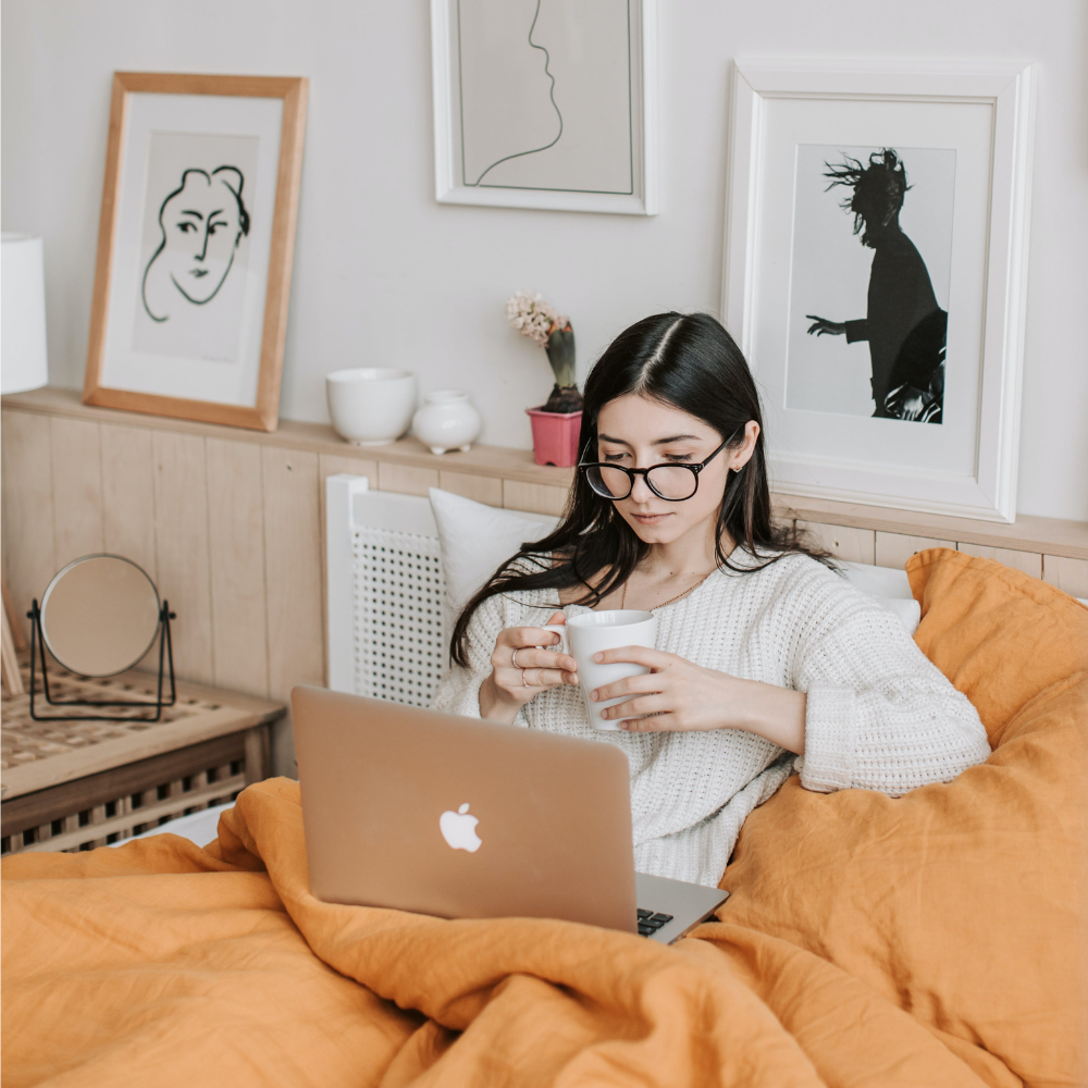 A woman with her laptop and coffee in bed