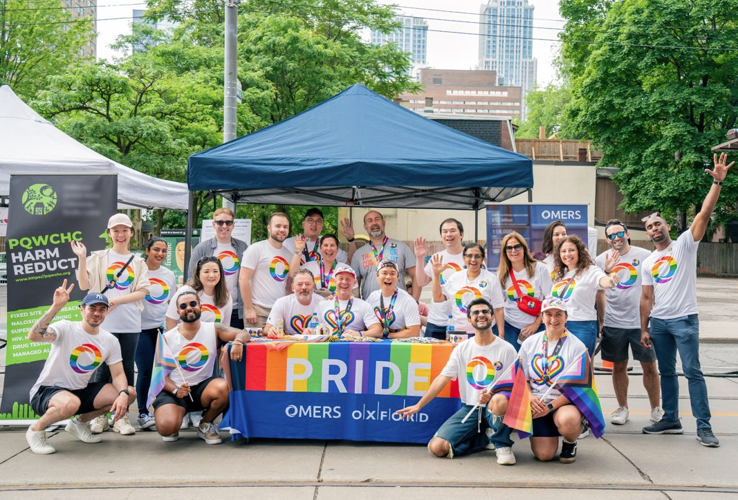A large group of people posing in front of a market booth for Pride