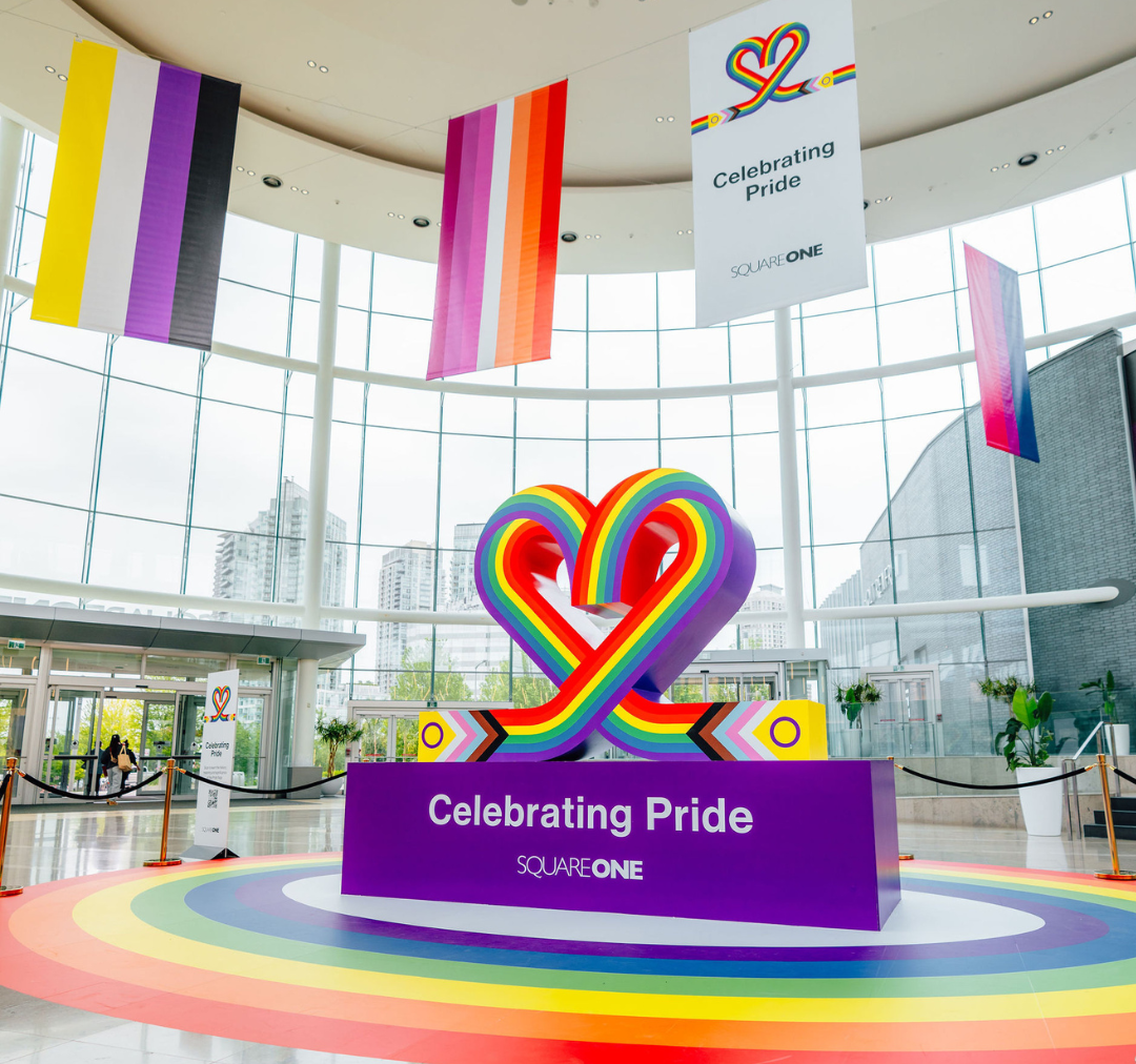 A rainbow heart on a purple pedestal with flags hanging in the background