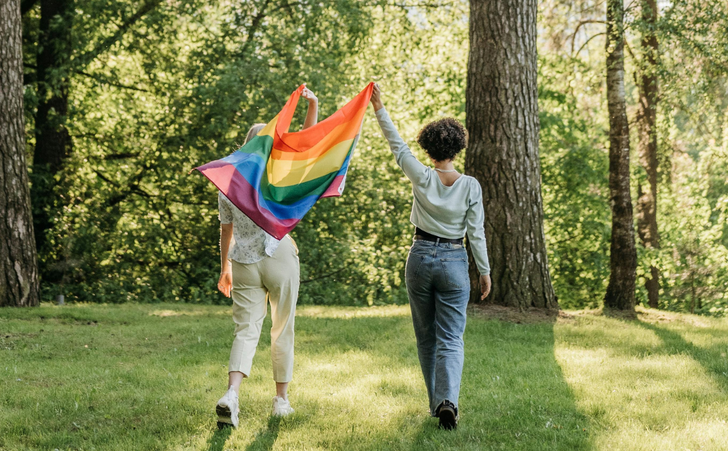 Two people holding up a Pride flag walking in a forest