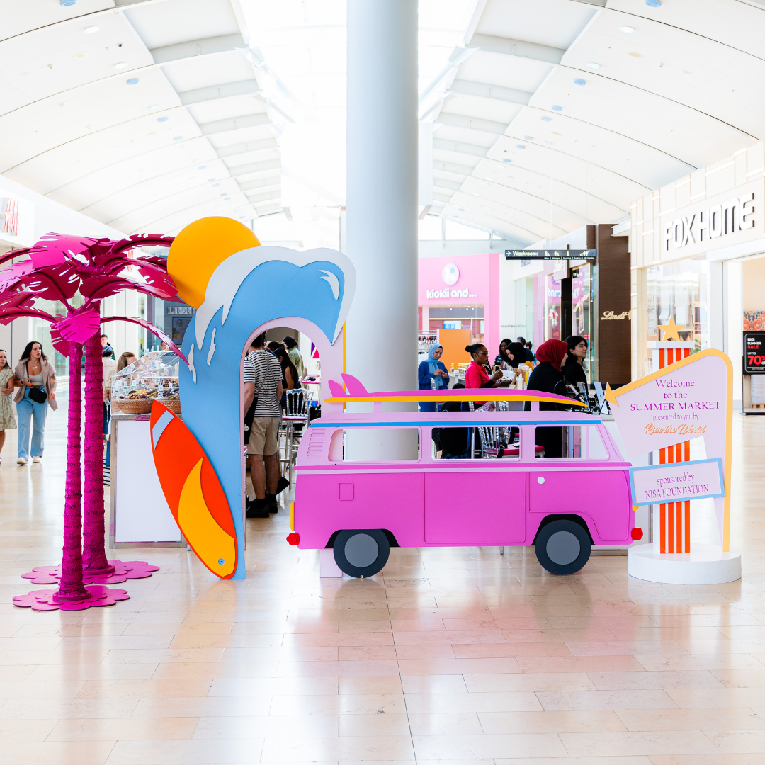 A summer themed installation featuring a pink van and palm trees