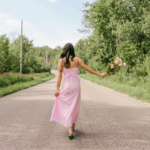 A woman in a pink dress holding a bouquet of flowers and walking down a road