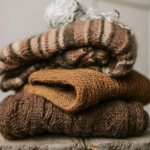 A pile of folded sweaters on a wooden stool