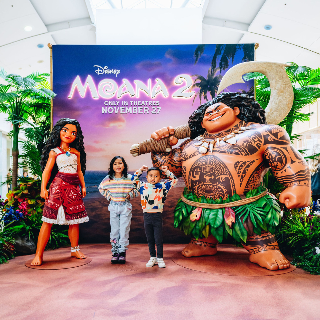 Two children standing beside life-sized Moana character statues