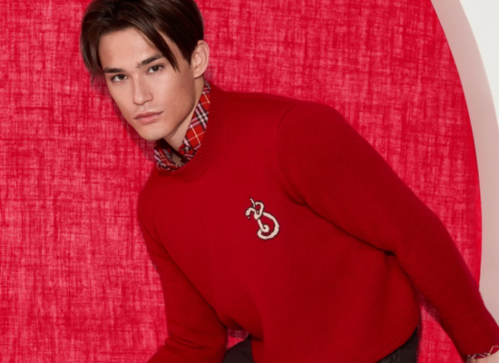 A man wearing a red crewneck sweater with a snake design on the left chest.