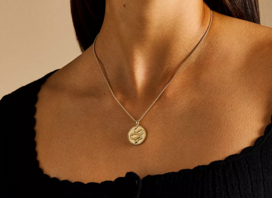 A woman wearing a gold pendant necklace with a snake design on it.