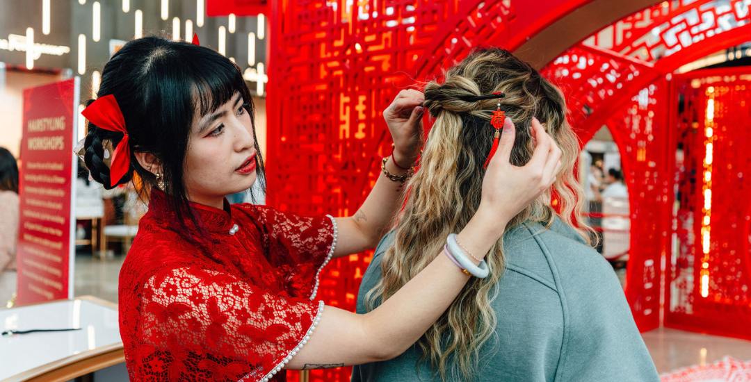 A woman dressed in traditional Chinese wear styling another woman's hair.