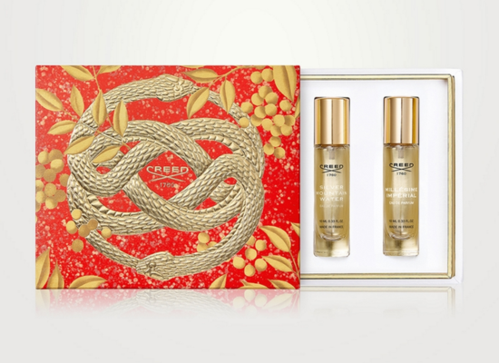 A red box with a gold snake design on it holding two perfume bottles.