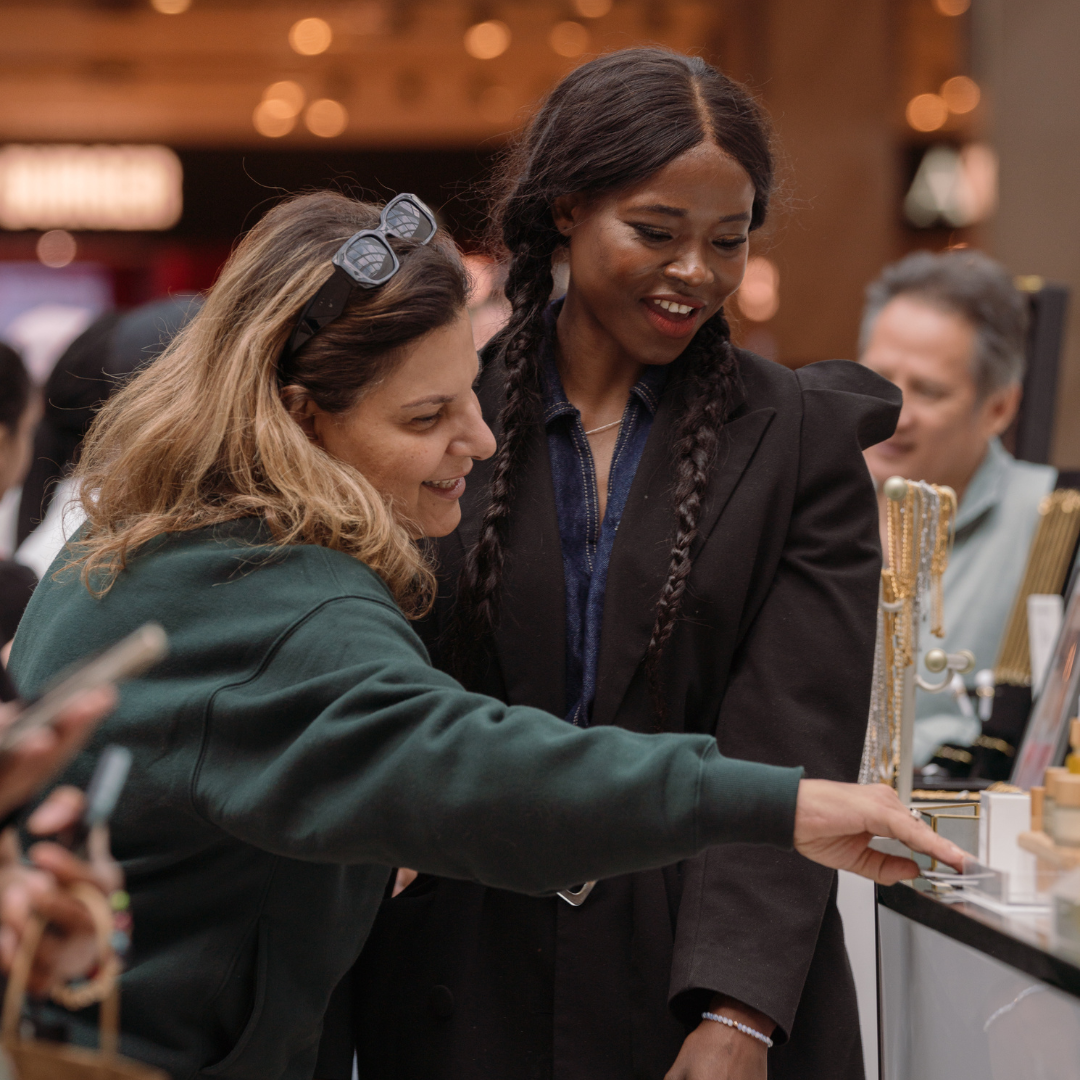 A woman showcasing her products at her market booth to another woman.