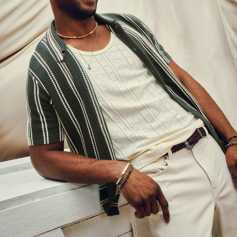 A man wearing a white tank top and a green striped short sleeve button up shirt.