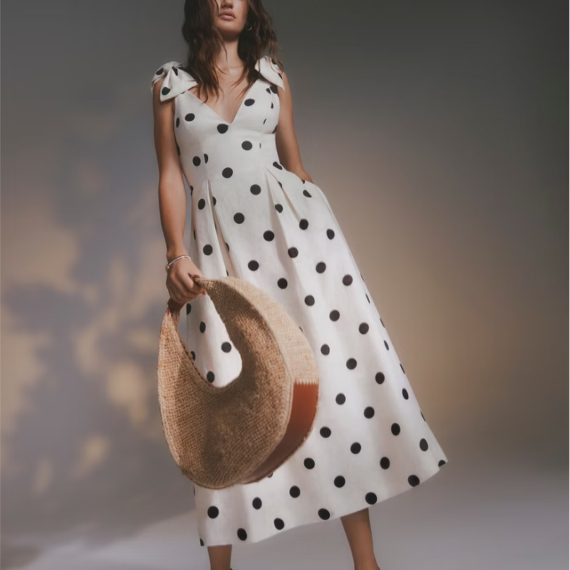 A woman wearing a spotted white dress and holding a woven bag.