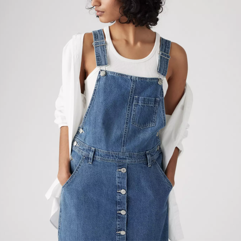 A woman wearing denim overalls and a white button up shirt.