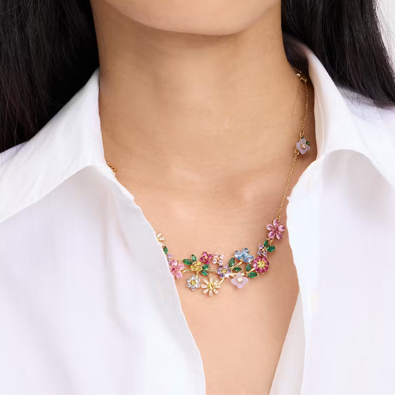 A woman wearing a gold necklace with floral pendant design.