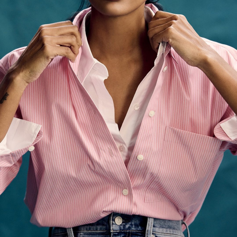 A person wearing a pink striped dress shirt tucked into a pair of jeans.