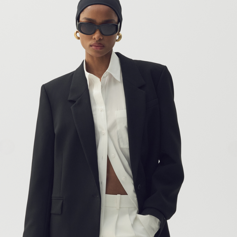 A woman wearing a black blazer, white dress shirt and white dress pants with sunglasses.