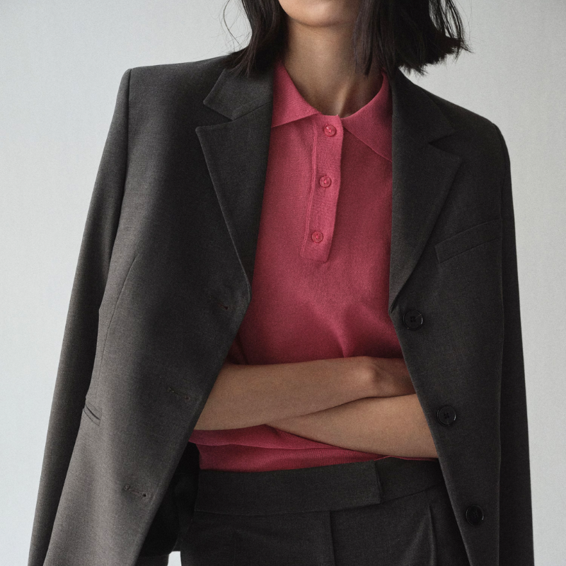 A woman wearing a dark grey blazer over a pink polo shirt.