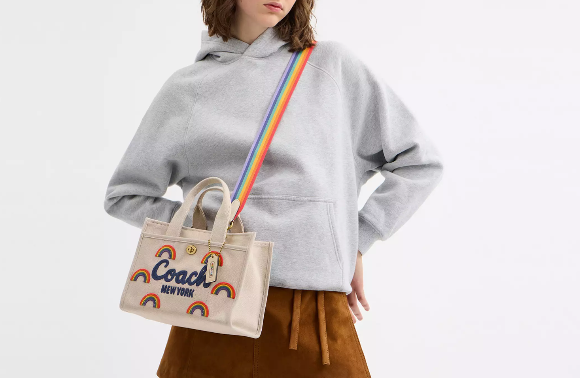 A woman wearing a handbag from Coach with a Pride themed design.