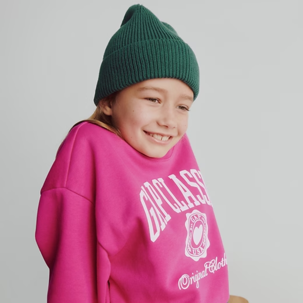 A girl wearing a pink Gap crewneck sweater and a green toque